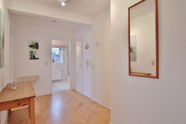 A hallway with a wooden floor, a wooden table, a mirror, and a door leading to another room.