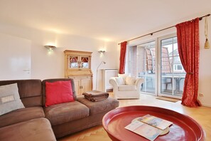 A living room with a brown sofa, a white armchair, a red coffee table, and a wooden cabinet.