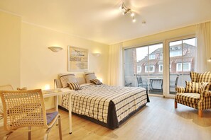 A bedroom with a bed, a desk, a chair, and a balcony with a view of buildings.