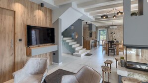 Interior moderno com uma TV fixada numa parede de madeira, uma escada que leva a uma cozinha e uma área de refeições com um balcão.