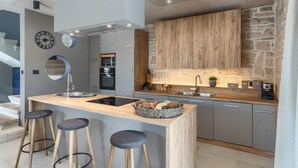 Uma cozinha moderna com ilha central, banquetas, parede de pedra e eletrodomésticos embutidos.