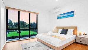 Un dormitorio moderno con un gran ventanal, una cama, una mesita de noche y un cuadro en la pared.