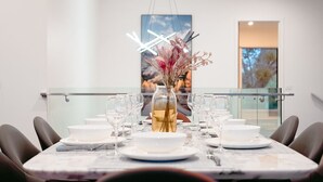 Mesa de comedor adornada con platos, tazones y copas de vino blancos, y centrada con un jarrón de flores.
