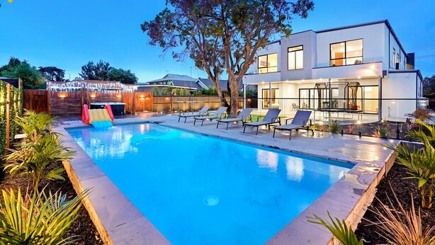 Una casa moderna de dos pisos con piscina, sillas de descanso y un tobogán.