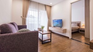 Moderni olohuone, jossa on sohva, sohvapöytä ja televisio. Viereisessä huoneessa on sänky.