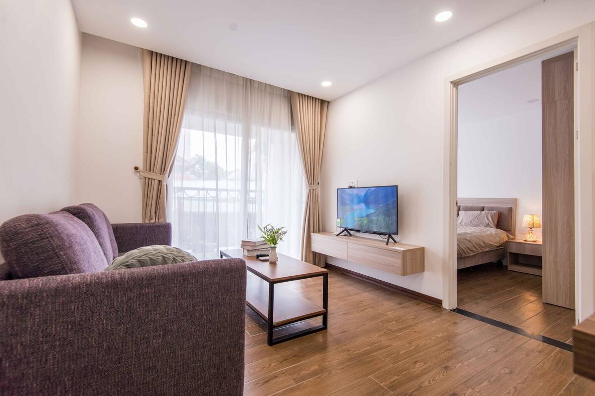 Ein modernes Wohnzimmer mit einer Couch, einem Couchtisch, einem Fernseher und einem Bett im angrenzenden Raum.