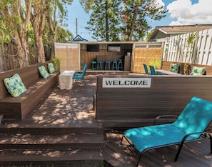 A wooden deck with a welcome sign, outdoor seating, and a covered area with chairs and tables. - Tiny House Calypso with 1st floor sleeping (Sarasota)