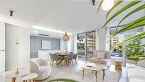A modern living room with a dining area, a sofa, and a coffee table. There is a large window with a view of the outdoors.