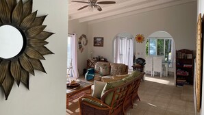 Ein großzügiger Wohnraum mit Deckenventilator, einem großen, sonnenförmigen Spiegel und Blick auf den Essbereich durch einen Rundbogen.