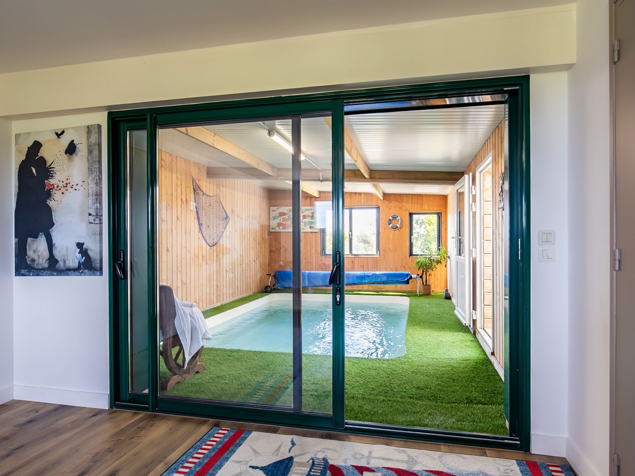 Una habitación con puerta corrediza de vidrio que da a una zona de piscina con césped artificial.