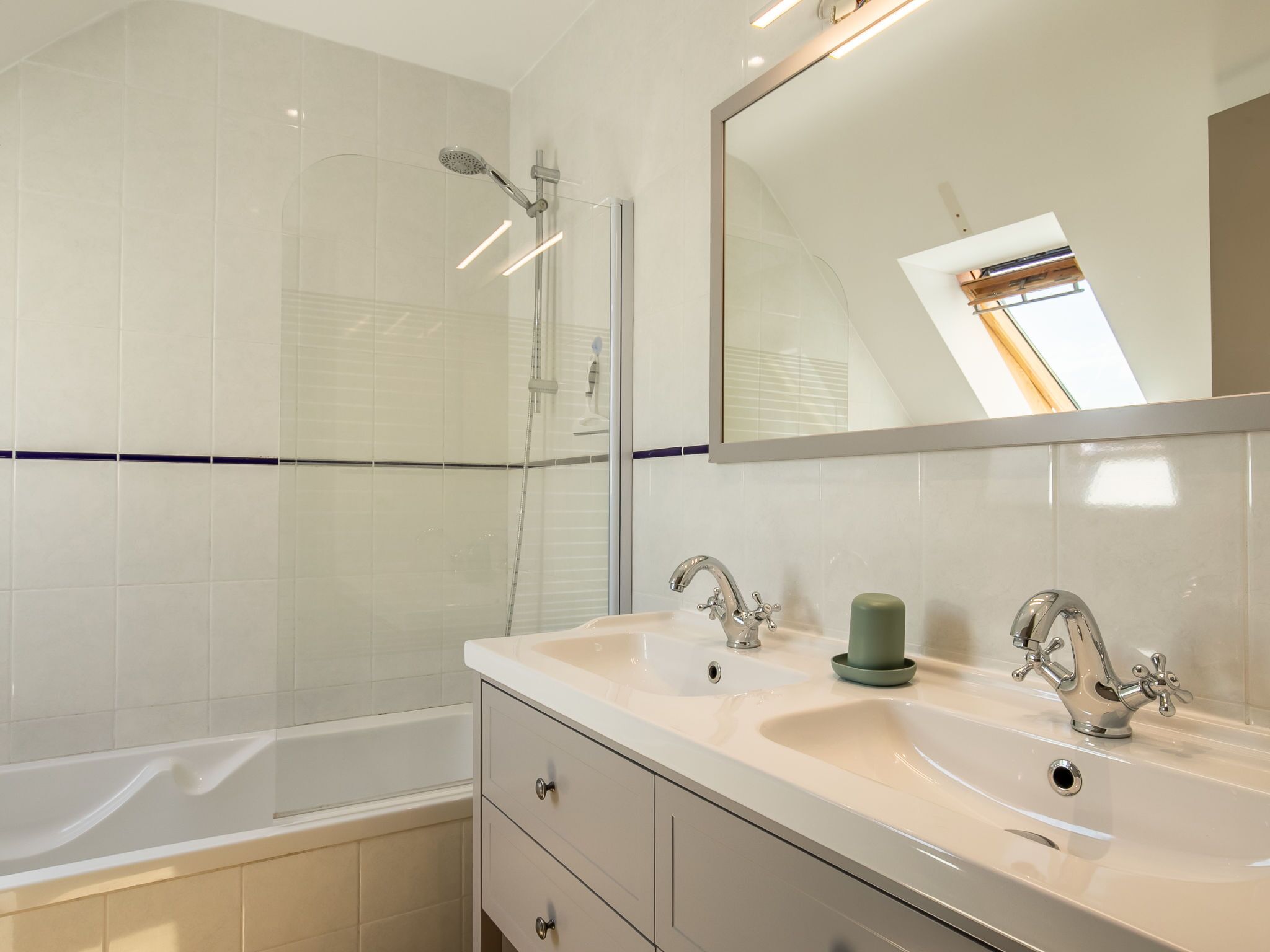 A modern bathroom with a bathtub, two sinks, a large mirror, and a skylight.