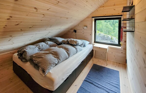 A cozy attic bedroom with a bed, a window with a view of greenery, and a small shelf.