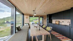 A modern kitchen with dark cabinetry, a wooden dining table, and a view of a green landscape through large windows.