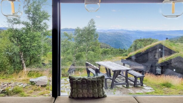 A modern interior with a large glass window offering a view of a mountainous landscape and rustic outdoor seating.