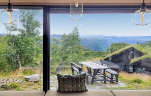 A modern interior with a large glass window offering a view of a mountainous landscape and rustic outdoor seating.