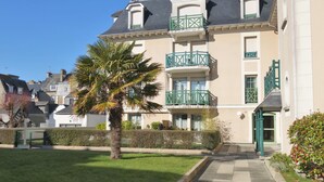 Un immeuble à plusieurs étages doté d’un balcon, d’un palmier et d’un chemin menant à l’entrée.