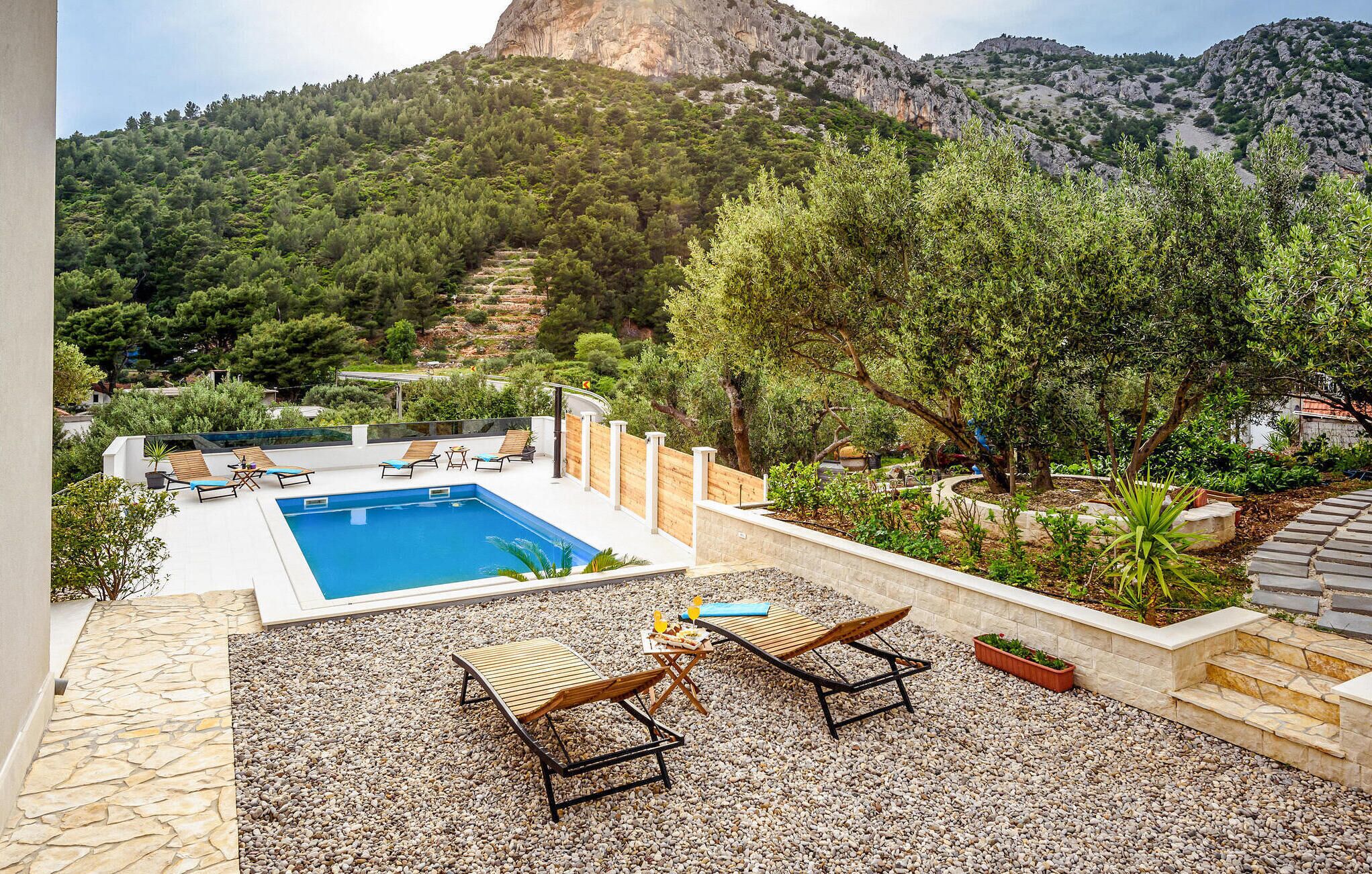 Un área de piscina en la azotea con sillones de descanso y una mesa, rodeada por un muro de piedra y guijarros.