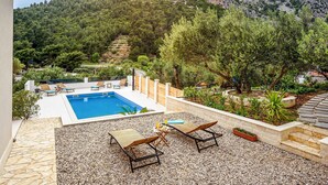 A rooftop pool area with lounge chairs and a table, surrounded by a stone wall and pebbles. - Nice apartment in Klek with WiFi (Klek)