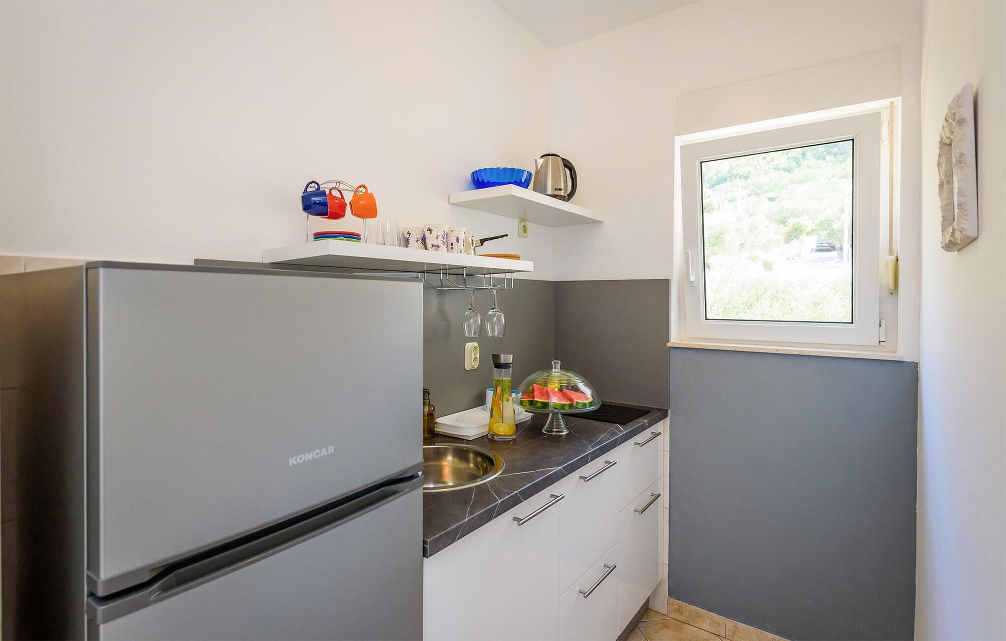 Una cocina compacta con un refrigerador, un lavamanos y una ventana.