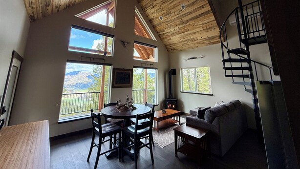 A spacious living area with a high ceiling, large windows offering mountain views, a fireplace, and a spiral staircase. - Cabin Retreat: Mountain Views, Starlink Wi-Fi, Stargazing, Hiking, Adventures! (Clinton)