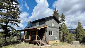 A two-story cabin with a wooden deck and a covered porch, surrounded by trees and mountains. - Cabin Retreat: Mountain Views, Starlink Wi-Fi, Stargazing, Hiking, Adventures! (Clinton)