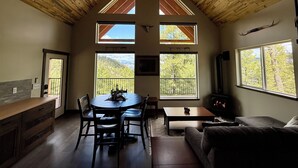 A cozy living room with a high wooden ceiling, a fireplace, and large windows offering views of the outdoors. - Cabin Retreat: Mountain Views, Starlink Wi-Fi, Stargazing, Hiking, Adventures! (Clinton)