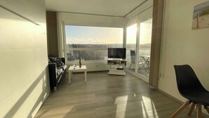 A modern living room with a large window, a flat-screen TV, a small coffee table, and a black chair. - Studioapartment in der Frische Brise 04.05 - Frische Brise (Cuxhaven)