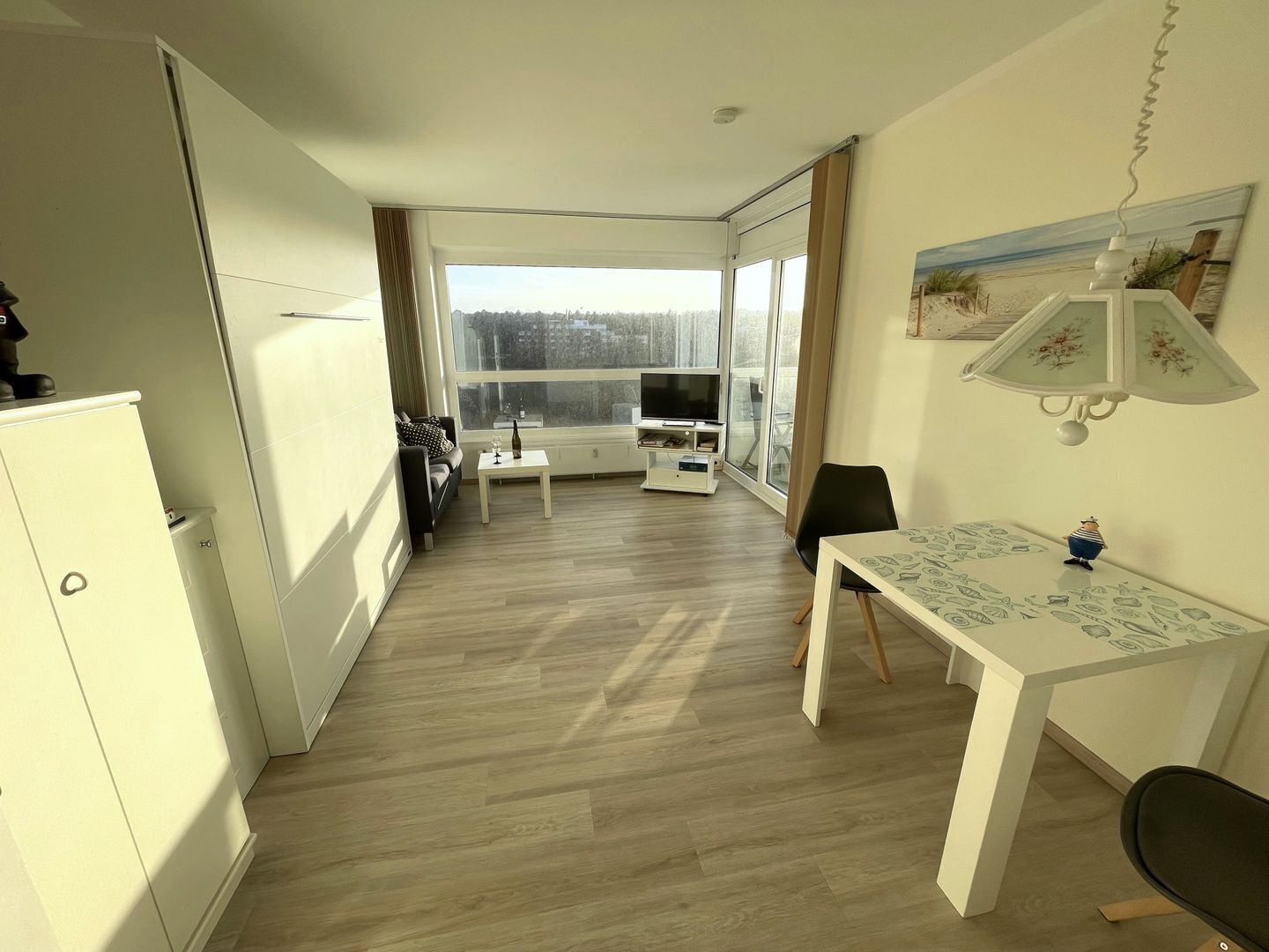 A modern apartment with a dining area, a TV, and a large window offering a view of the city.