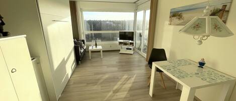 A modern apartment with a dining area, a TV, and a large window offering a view of the city.