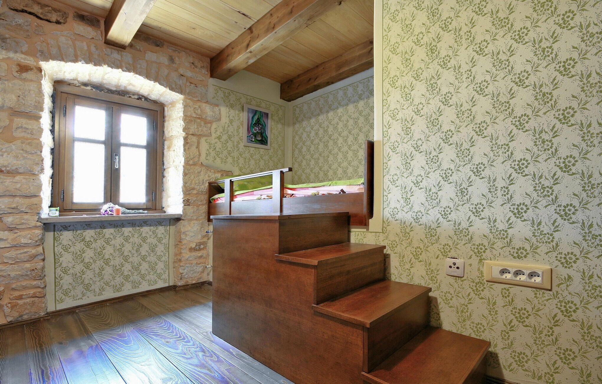 A room with a wooden staircase, a stone wall, a window, and floral wallpaper.