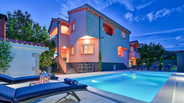 Una casa moderna de dos pisos con piscina, mobiliario exterior y una escalera que lleva al piso superior.