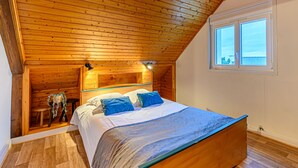 Una camera da letto con soffitto in legno, un letto con cuscini blu e una finestra vista.