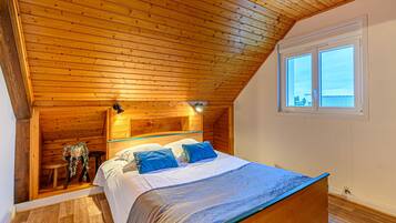 Une chambre avec un plafond en bois, un lit avec des oreillers bleus et une fenêtre donnant sur un beau paysage.