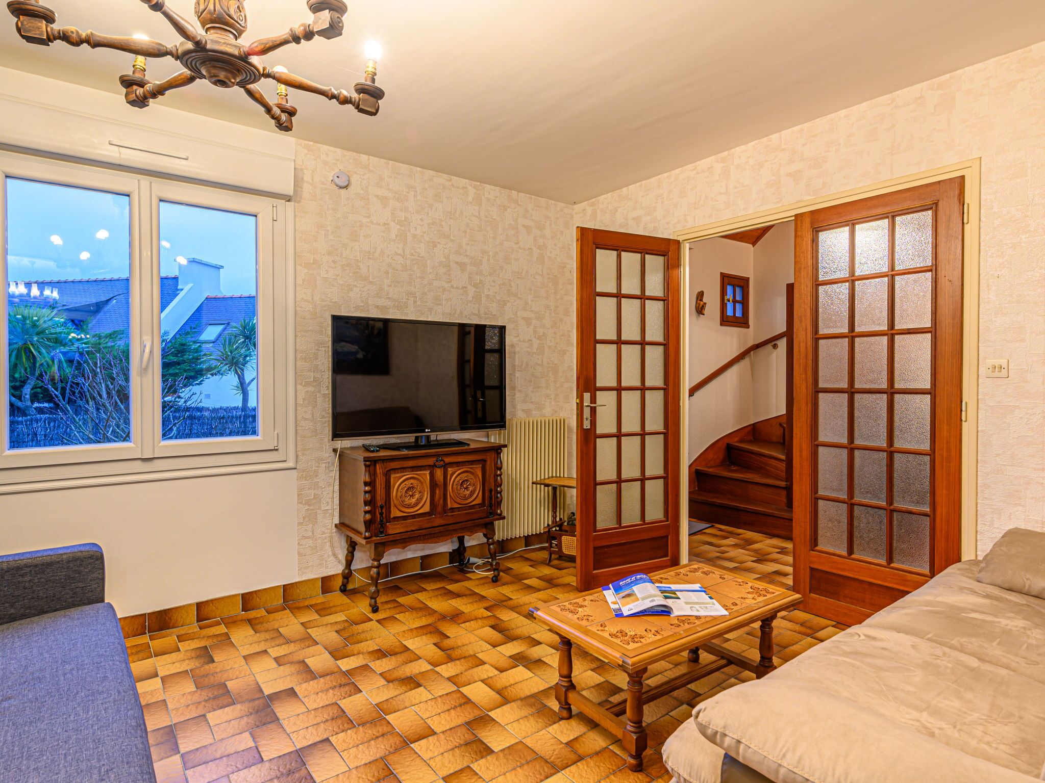 Un salon avec un téléviseur, des meubles en bois, un parquet à motifs et une vue par la fenêtre.