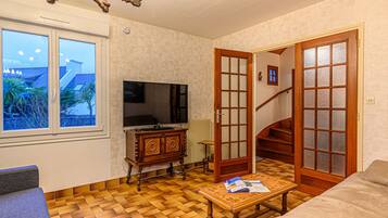 Un salon avec un téléviseur, des meubles en bois, un parquet à motifs et une vue par la fenêtre.
