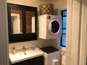Une salle de bain compacte équipée d’un lave-linge intégré, d’un lavabo avec distributeur de savon et d’une fenêtre donnant sur un paysage agréable.
