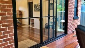 A room with a large sliding glass door leading to an outdoor area with a wooden deck and a chair. - The Bungalow - Luxurious & Calm | Beach & Bush (Valla Beach)