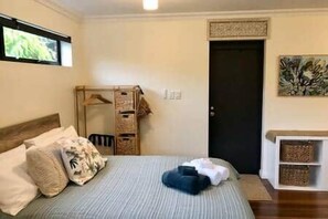 A bedroom with a bed, a hanging laundry rack, a door, and a shelf with baskets. - The Bungalow - Luxurious & Calm | Beach & Bush (Valla Beach)