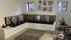 A modern living room with a sectional sofa, a coffee table, and a rug. There are framed artworks on the wall and a potted plant on a side table.