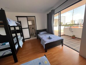 A room with a bunk bed, a single bed, a bathroom, and a balcony with a view of the city. - Epifania Guest House (Cali)