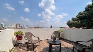 A rooftop terrace with tiled flooring, two plastic chairs, a small round table, and potted plants.