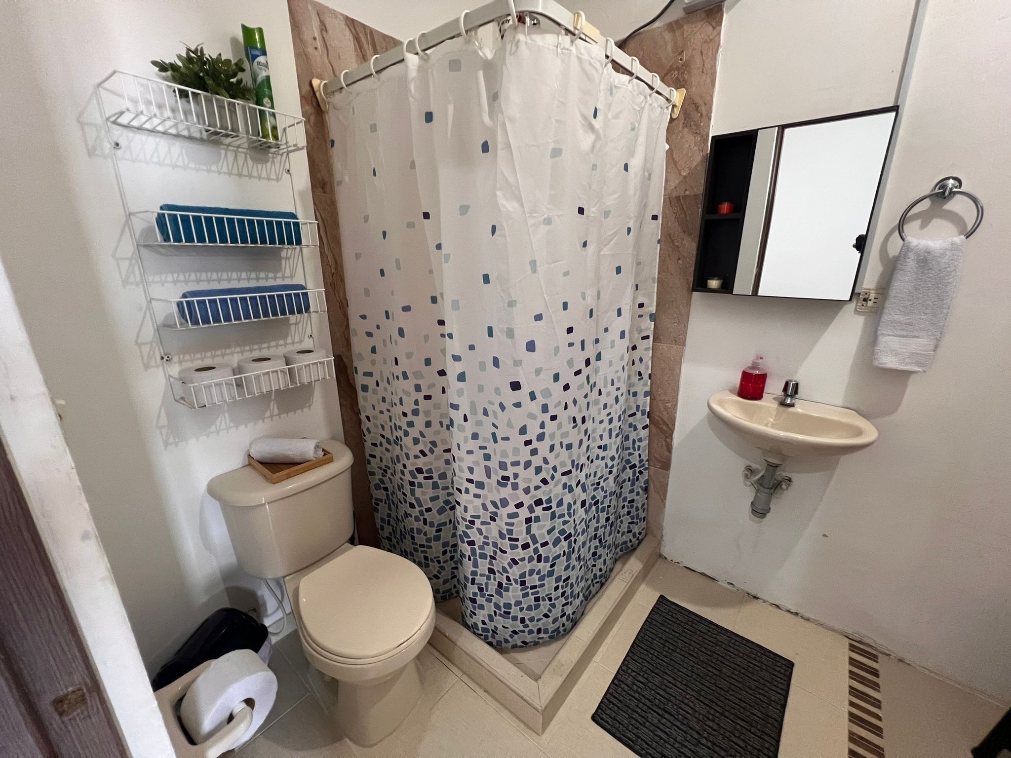 A small bathroom with a toilet, a shower curtain, a sink, and a shelf with toiletries.
