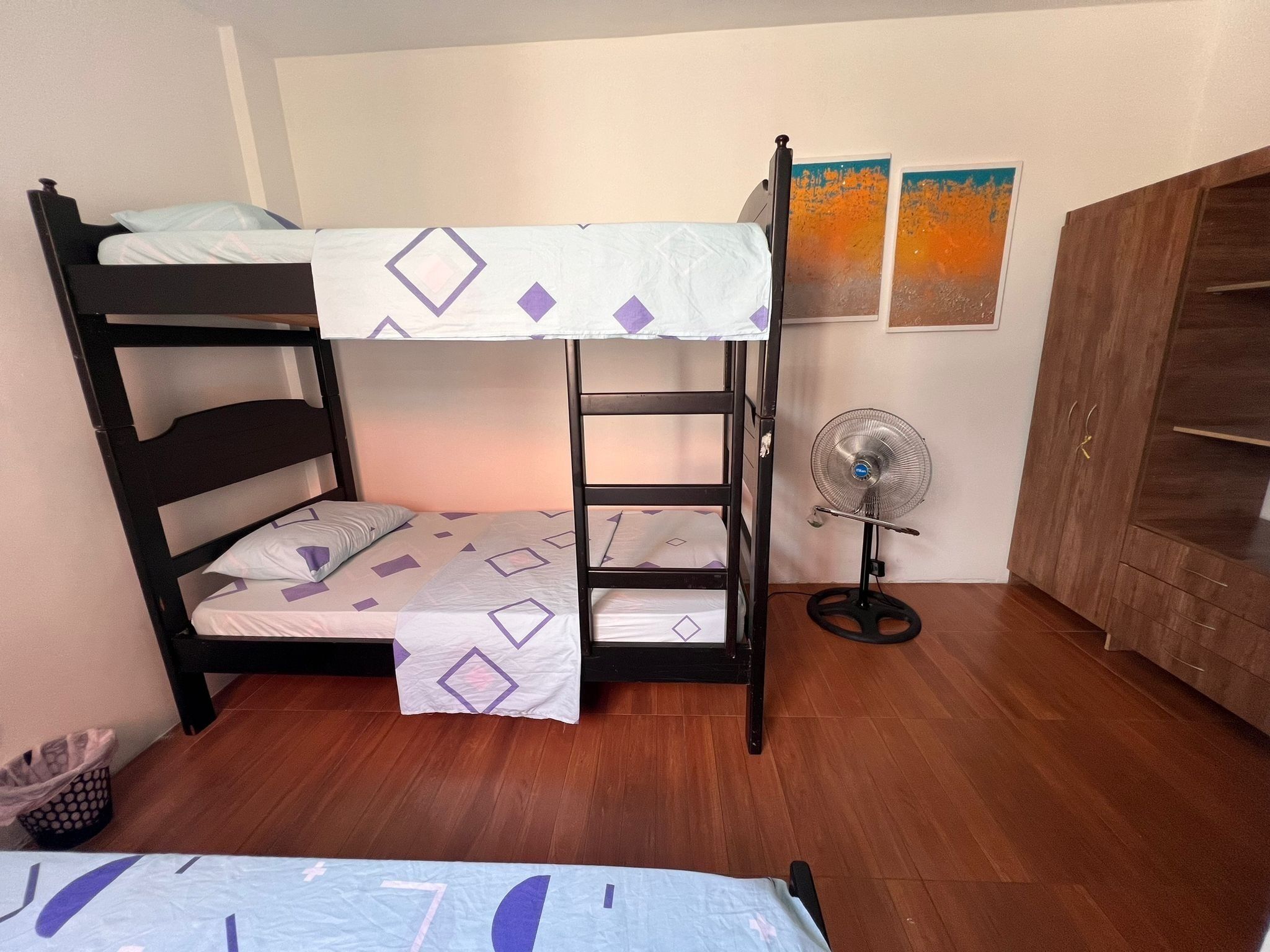 Una cama litera con escalera, un ventilador de pie y un armario de madera.