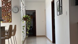 A spacious hallway with a dining area featuring wicker chairs and a hanging plant.