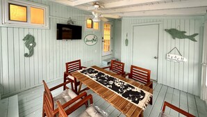 A dining area with a wooden table and chairs, a ceiling fan, and a wall-mounted TV.