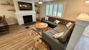 A modern living room with a fireplace, a sectional sofa, a round coffee table, and a dining area with chairs.
