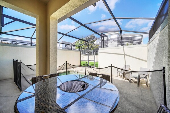 A glass-enclosed outdoor seating area with a round table and chairs, surrounded by a rope barrier.