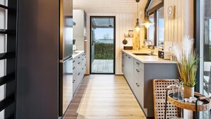 Een moderne keuken met houten kastjes, een groot raam en uitzicht op groen.
