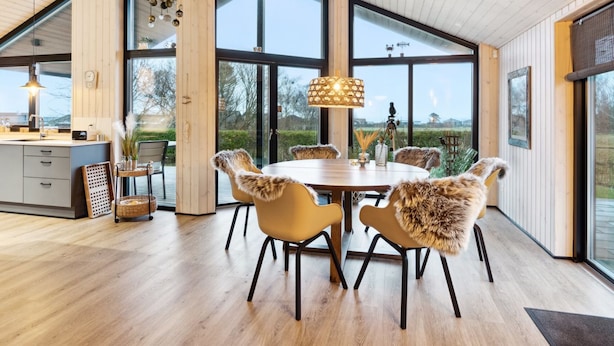 Een moderne eetruimte met een ronde tafel en stoelen, grote ramen en een houten plafond.