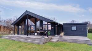Een modern huis met een grote glazen uitbouw, een terras en een aparte garage.